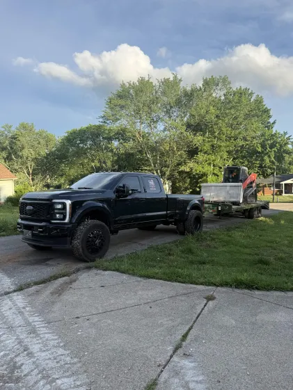 TCS Land Management truck hauling a mini excavator on a trailer